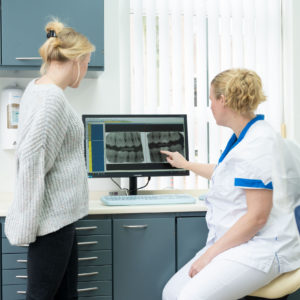 twee vrouwen kijken naar röntgenfoto om te kijken of de klant een gaatje heeft in tand of kies